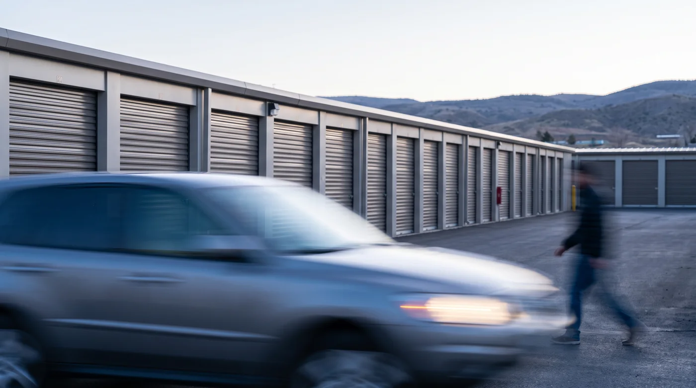 A self-storage facility at dusk, a car and customer passing the unit doors